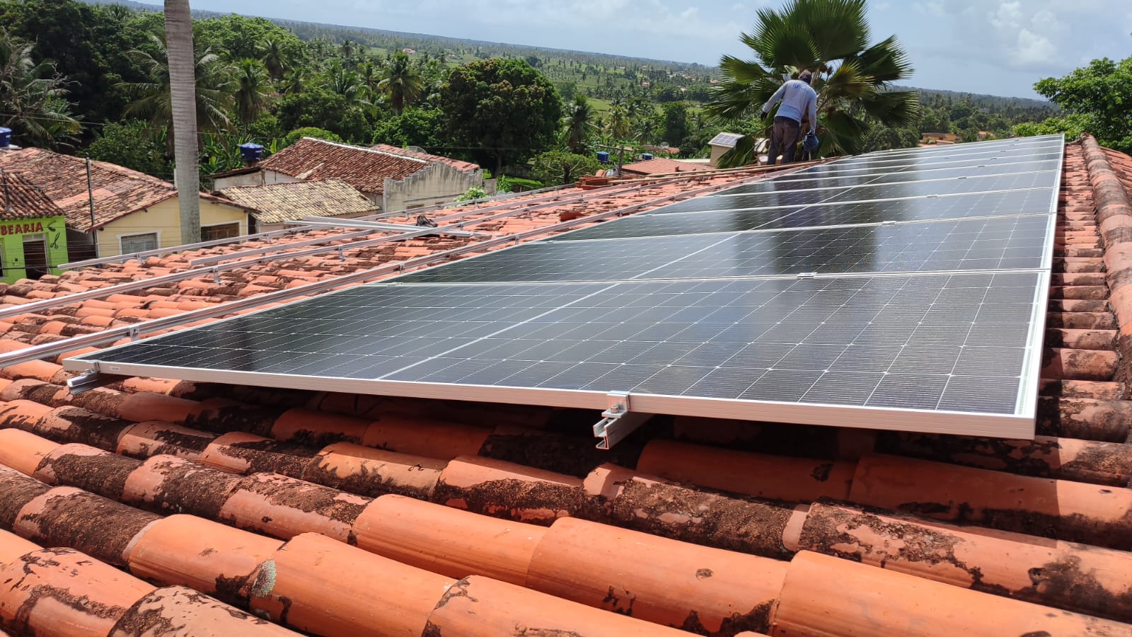 Placas solares recém-instaladas em um telhado residencial, com técnico ao fundo.